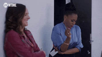 TV gif. Molly Shannon as Jackie and Jenifer Lewis as Patricia in I Love That For You. Both women are smoking outside and Patricia leans back and looks at Jackie as she laughs, cracking up at her friend's words.