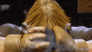 Video game gif. From "Street Fighter 6," Ken Master falls to his knees on a dusty surface, bowing his head, holding one fist to open palm as dust flies up around him from the impact. 
