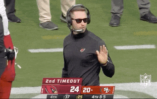 Sports gif. Standing at the sidelines wearing sunglasses and a headset, Cardinals coach Kliff Kingsbury nods and gives a thumbs up.