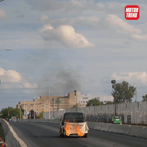 Video gif. Modified vehicle on a closed race course shoots a tall pair of flame jets straight up towards the sky.