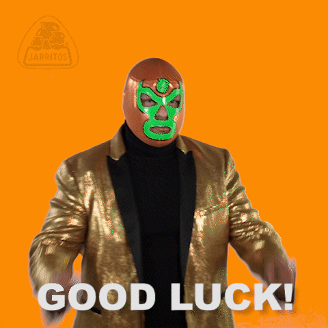 Ad gif. In a Jarritos ad, a Lucha libre wrestler in an orange and green face mask and gold suit holds up two hands, crossing his fingers. Text, “Good luck!”