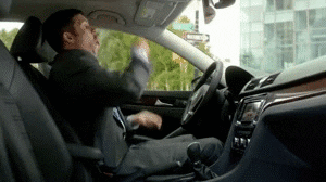 Man in car doing air drumming in front of steering wheel.