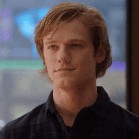 TV gif. Lucas Till as Mac on MacGyver smiles, blinks, and nods his head modestly.