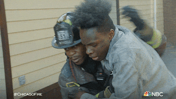 TV gif. A firefighter helps a man as they run away from a flaming building on Chicago Fire.