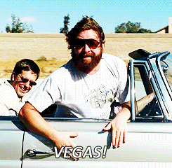 Muž jedoucí v autě, ukazující směrem k pozorovateli gifu s nápisem "Vegas!". 