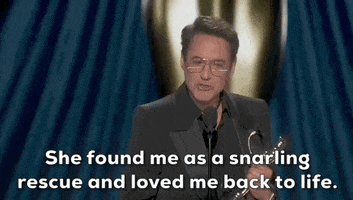 Oscars 2024 gif. Robert Downey Jr wins Best Supporting Actor. He holds the Oscars trophy sideways. He gives appreciation to his wife by saying, "She found me as a snarling rescue and loved me back to life."