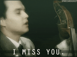 Music video gif. Mark Hoppus of Blink 182 in the I Miss you Music Video closes his eyes as he sings and plays the upright Bass. There’s a faded version of him in the background that’s also singing and bopping his head to the beat. Text, “I miss you.”