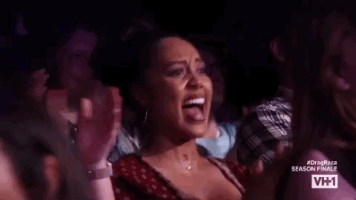 Reality TV gif. Audience members of RuPaul's Drag Race clapping and getting hyped up while smiling.