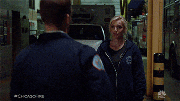 Tv gif. Kara Killmer as Sylvie Brett on Chicago Fire stands in front of a fire hall with an ambulance parked in the garage and Jesse Spencer as Matthew Casey runs up to her, caresses her neck, and they passionately kiss each other.