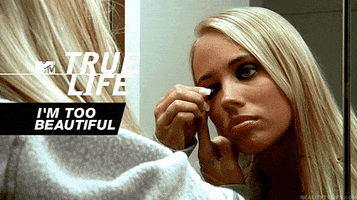 Reality TV gif. A woman on MTV True Life looks in a mirror and holds her eyelid as she applies dark eyeshadow with a brush.