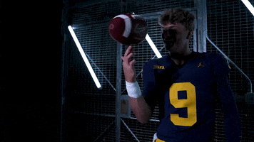 Video gif. Football player smiles and twirls a football on his index finger.