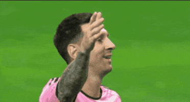 Sports gif. Lionel Messi smiles hopefully with his arm raised, but turns away and puts his palm on his head when he sees that he didn't score. 
