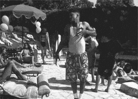 Celebrity gif. Black and white clip of Will Smith purposefully falling into an empty lounge chair next to a beautiful woman at a pool.