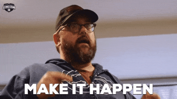 TV gif. A scene from Movie Trivia Schmoedown. Wearing a black baseball cap and a dark blue hoodie, a serious Drew McWeeny gestures with his pointer fingers as he tells us to: Text, "Make it happen."