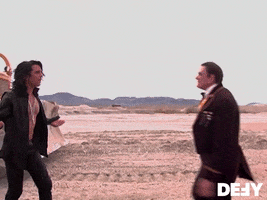 Video gif. Burly man in a suit comes up to Criss Angel and punches him in the face, sending Criss to the ground.