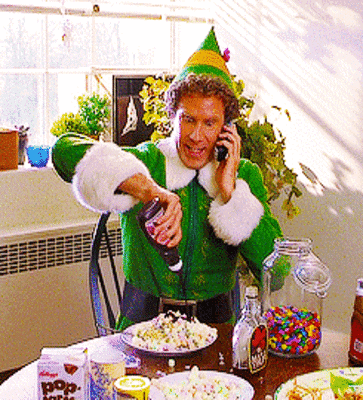 Movie gif. Will Ferrell as Buddy in Elf. He is sitting at a table with candy and sugar all around. He's eagerly squirting chocolate sauce all over his popcorn as he talks on the phone.