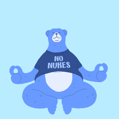 Digital art gif. Cartoon blue bear wearing a shirt that says, "No Nukes," sits with its legs bent on the ground, its paws curled into a meditation pose. A rainbow forms over the bear's head, text inside of which reads, "Be calm, don't bomb," all against a baby blue background.