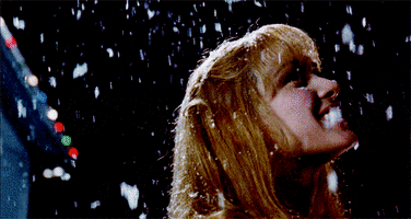 Movie gif. Winona Ryder as Kim in Edward Scissorhands looks up, smiling and twirling around as powdery snow falls down.