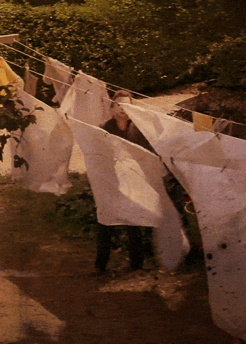 Movie gif. The masked Michael Myers in Halloween gazes towards us as he stands among billowing sheets that hang on a laundry line.
