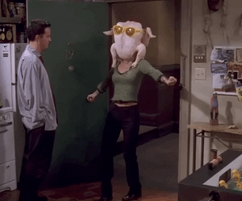 An animated gif from the TV show Friends. Monica has a raw turkey on her head with giant sunglasses on it and is doing a silly shimmy dance for Chandler.