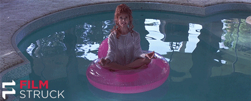 An animated gif clip from the movie Mars Attacks with Annette Benning sitting on a floatie in the middle of a pool in a meditation pose with a big smile on her face