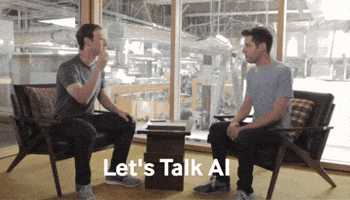 Dois homens sentados em um ambiente moderno, conversando. O texto "Let's Talk AI" aparece na parte inferior da imagem.