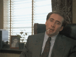 Movie gif. Nicholas Cage as Peter in Vampire's Kiss leaning forward from an office chair with a cigarette hanging out of his mouth, pointing out excitedly.