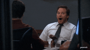 Parks and Recreation gif. Chris Pratt as Andy is sitting at a dining table and looks intensely excited at something he hears, his eyes widening hughley and his mouth wide open. We zoom in on him as he continues to look excited.