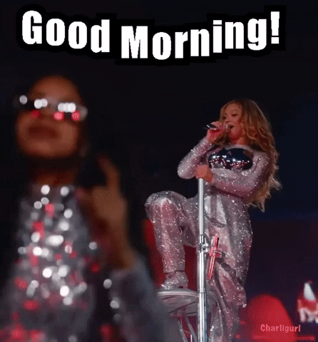 Video gif. Blue Ivy Carter on stage wearing sunglasses and a sparkly silver top as she points at the corners of her mouth and smiles. Beyonce sings into a microphone in the background. Text, "Good morning!'