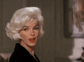 Movie gif. In slow-motion, Marilyn Monroe licks her lips as she turns toward us.