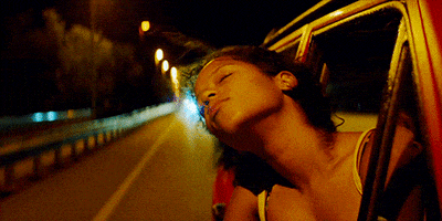 Movie gif. Taylor Russell as Emily in Waves. It's nighttime and she's in the passenger seat of a car with her head out of the window. Her eyes are closed and her hair is whipping in the wind as she seems to be soothed by the night air.