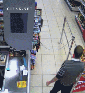 Video gif. Surveillance footage from a security camera on the ceiling shows the check out line. A man attempts to jump over a chain blocking the lane, but trips on the chain on the way up, falling, and bringing a shelf of merchandise down on top of him as he falls.