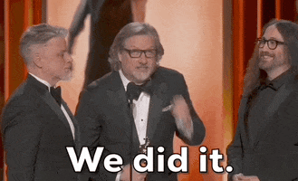 Oscars 2024 GIF. Dave Mullins holds up his Oscar on stage and he looks up into the sky and pumps his award up, celebrating his win and thanking the audience. 