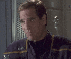 TV gif. Scott Bakula as Jonathan in Star Trek: Enterprise. He's chewing food and listening to a story that makes him smile with his mouth closed.