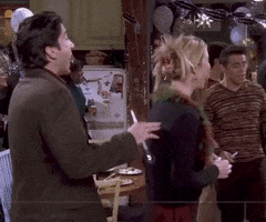 TV gif. Lisa Kudrow as Phoebe in "Friends" spins around to smile at David Schwimmer as Ross. Behind them, a bunch of friends including Rachel and Joey hug and ring in the New Year. Text, "Happy New Year!'
