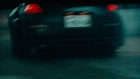 Movie gif. A street racing car from Fast and the Furious speeds up a circular parking garage ramp. Smoke emits from under it as it drifts around a tight concrete ramp. 