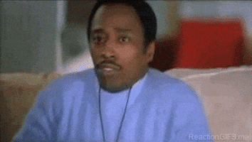 Movie gif. Wearing a light blue shirt and a necklace, Eddie Griffin watches something offscreen with interest while eating popcorn.