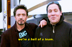 Celebrity gif. Robert Downey Jr leans on the shoulder of Jon Favreau, standing outside of a trailer, and says, "we're a hell of a team,' which appears as text. Caption: "2010, from the set of Iron Man 2."