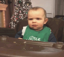 Video gif. A baby in a high chair with a confused expression on his face lights up with inspiration. He raises his hand, index finger extended as if to share his bright idea.