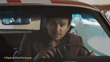 Movie gif. Josh Hartnett as Danny in Operation Fortune: Ruse de Guerre sits in a classic car, holding the steering wheel as he smiles and gives us a thumbs up.