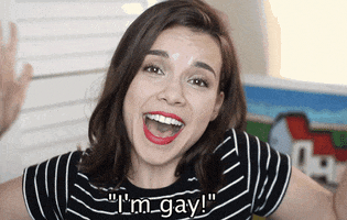 Video gif. Woman looks exhilarated as she puts her hands in the air and announces, "I'm gay!"
