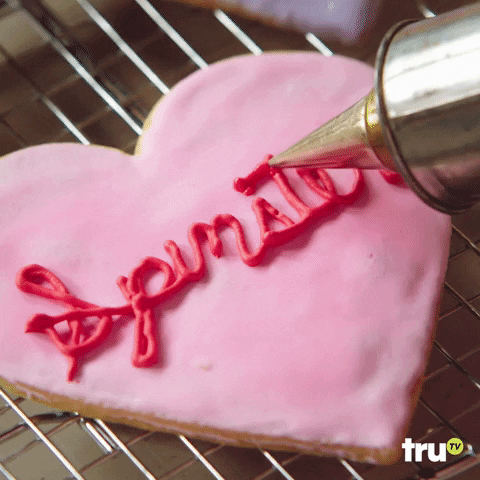 Gif of a heart-shaped cooking with pink icing as the word 'spinster' is being piped onto it. 