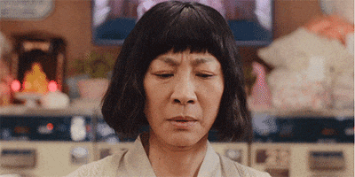 Movie gif. Michelle Yeaoh as Evelyn in Everything Everywhere All At Once with short cropped hair and bangs gives a confused or surprised look as she raises her hands in front of her face with fingers that have transformed into long, noodley, skin-colored hot dogs.