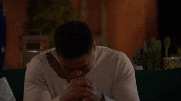 Reality TV gif. In a scene from The Bachelorette, a disappointed contestant in a gray sweatshirt hunches over with his head on his hands.