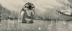 Cartoon gif. Stitch from Lilo and Stitch looks heartbroken, lip quivering while standing in a puddle in the rain. The scene has a dramatic sepia-tone filter over it.