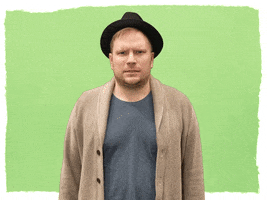 Celebrity gif. Wearing a black fedora, Patrick Stump from Fall Out Boy gives us a confused look as four question marks pop up around his head.