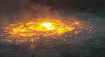 Video gif. An underwater gas pipeline leak burns with an orange glow in the waters of the Gulf of Mexico.