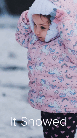 Video gif. Toddler adjusts their hood then stands stiff in her extremely puffy pink unicorn jacket. White text reads, “It Snowed.”