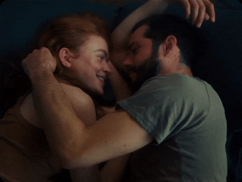 Movie gif. Sadie Sink as Her and Dylan O'Brien as Him in All Too Well lie facing each other as they caress each others faces with affection. 
