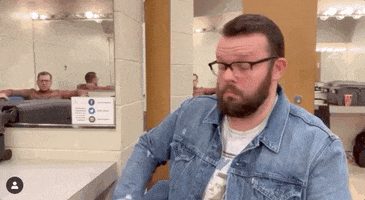 Celebrity gif. Zoom in on Aaron Chewning in a denim jacket, blinking and tilting his head as if trying to make sense of surprising news.